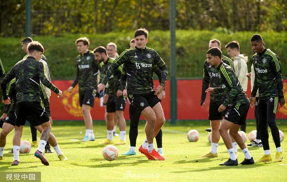 全体曼联队员围成一圈进行拉伸训练，背景是经典的卡灵顿训练基地，展现了团队的整体性与纪律性。