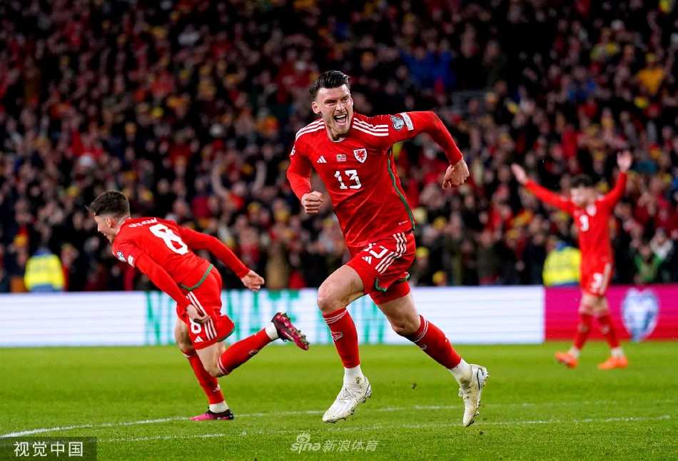威尔士队长拉姆塞中场控球，拉脱维亚两名球员上前夹抢，背景是满座的红色看台，气氛热烈。