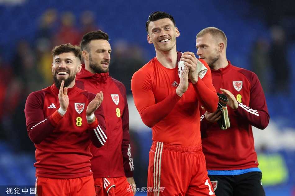 威尔士进球功臣穆尔张开双臂奔向角旗区疯狂庆祝，背景中助攻的詹姆斯正兴奋地跃起，队友们从四面八方涌来。