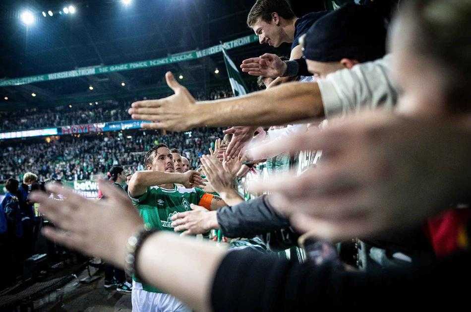 一群身着红色助威服的球迷在看台上臂挽着臂，齐声呐喊，气势如虹