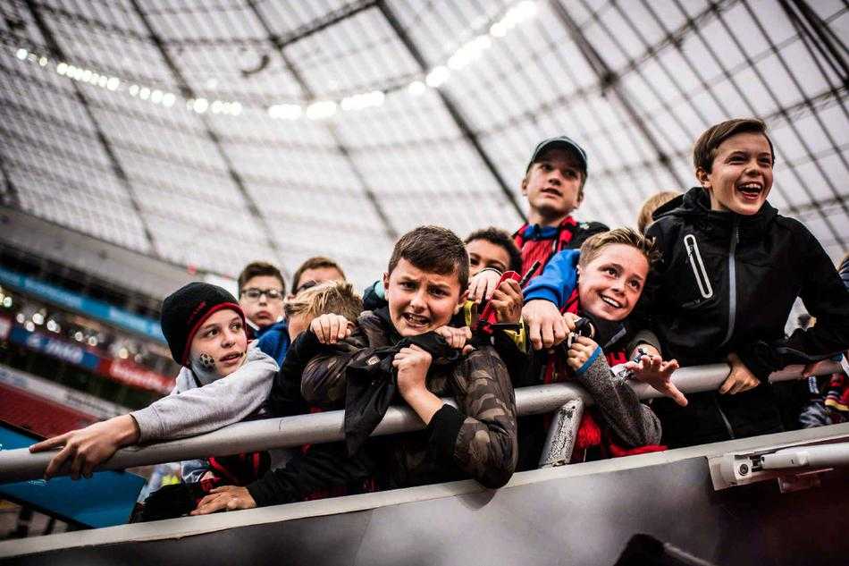 一位老球迷身披国旗，神情专注而坚定，岁月在他的脸上刻下了痕迹，但眼中对足球的热情从未熄灭