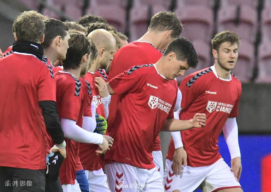 丹麦国家队球员在赛前合影中，整齐划一地身穿醒目的红色定制T恤，他们神情专注而坚定，T恤上‘Football Supports Change’的白色标语在球场灯光下熠熠生辉，向世界传递着超越体育竞技的人道主义呼声。