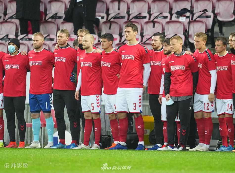 镜头拉近，可以清晰地看到丹麦球员身上T恤的细节，白色的‘Football Supports Change’字样简洁有力。球员们的目光凝视着前方，仿佛在无声地追问，他们无声的站立构成了一道超越比赛本身、充满力量的宣言墙。