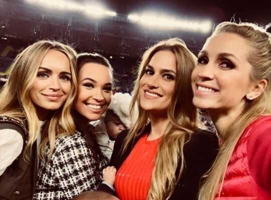 在诺坎普球场的一个家庭包厢内，一位金发女士抱着孩子，与周围的人一同俯瞰着场内激烈的比赛。她的眼神中既有对家人表现的期待，也充满了作为母亲和妻子的温柔与自豪。