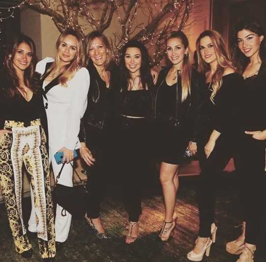 夜色下，一位女士身着一袭闪亮的礼服，佩戴着精致的珠宝，仿佛从红毯上走来。她对着镜头露出迷人的微笑，身旁的足球运动员男友则满眼爱意地看着她，画面充满了明星夫妇的气场。