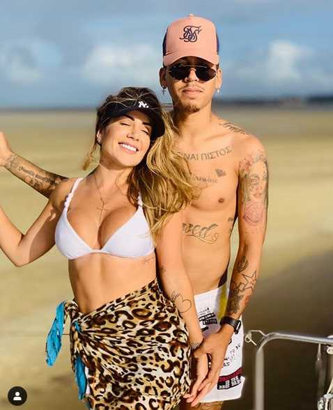 拉丽莎身着剪裁利落的黑色西装套装，内搭简约白T，干练又时髦。她单手插兜，站在街头，眼神自信地直视镜头，气场十足，完美诠释了现代独立女性的魅力。